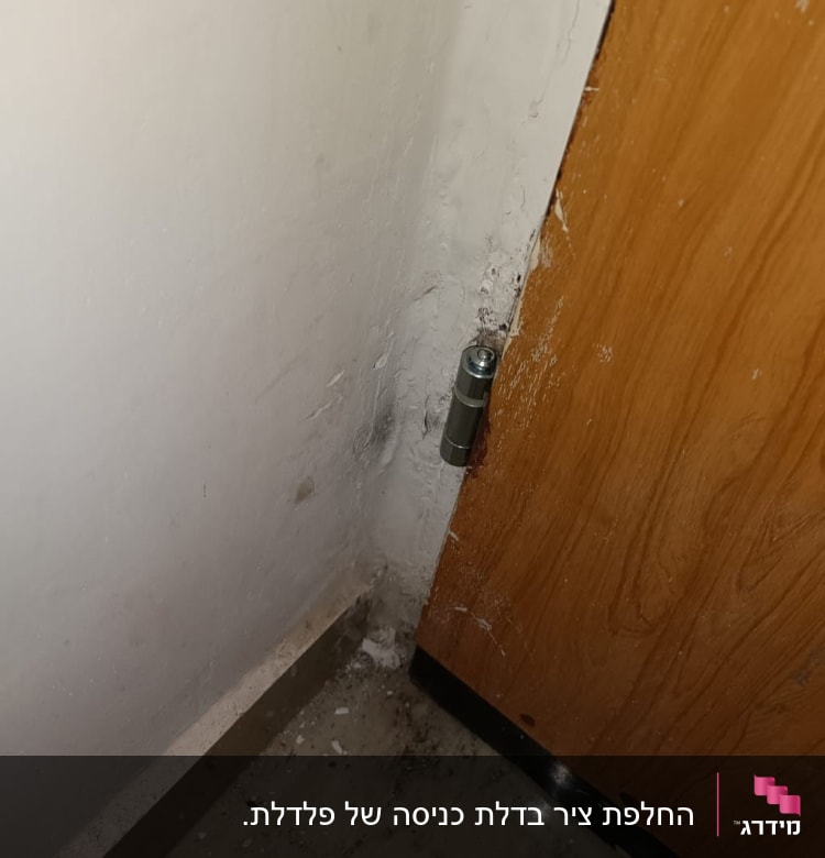 ציר מתכת בדלת עץ ליד קיר לבן